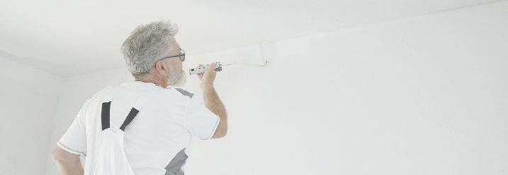 Ein Malermeister streicht die Kante zwischen Zimmerdecke und Wand.